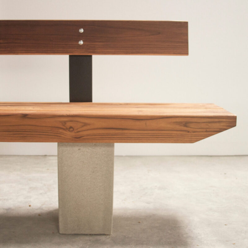 Banco B wooden bench by Gola Home, featuring diagonally cut wood slats, concrete block legs, and a wood backrest with metal supports, handcrafted in the Dominican Republic.