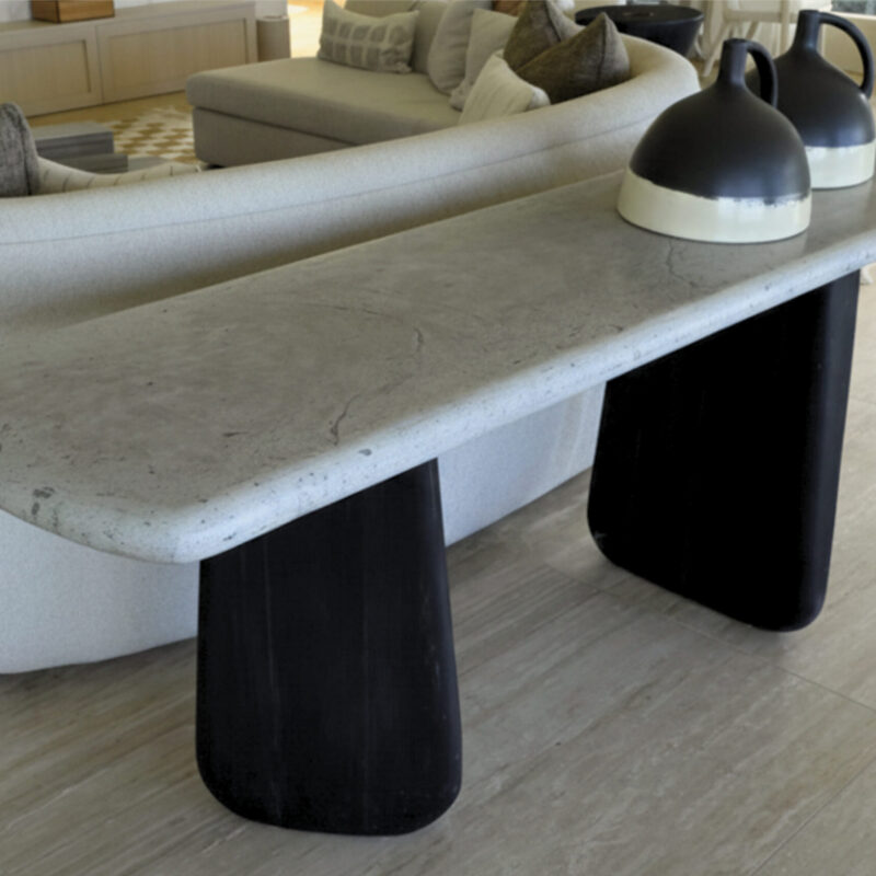 Organic console table with asymmetrical burnt wood legs and a rectangular polished concrete top with curved edges, perfect for modern interiors.