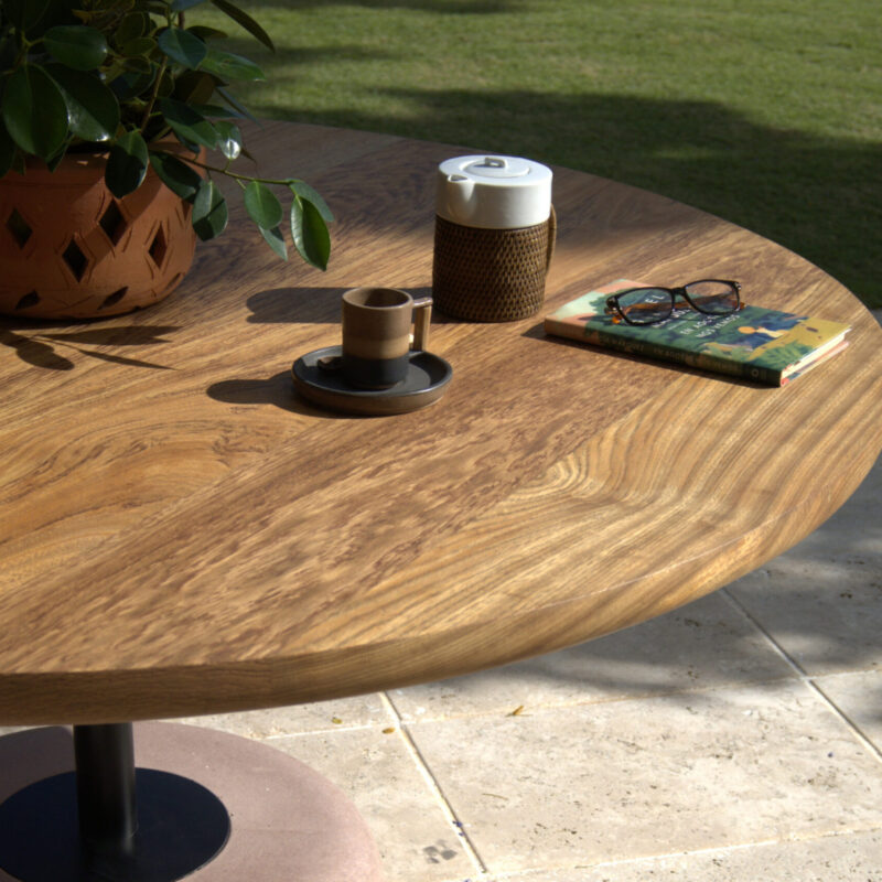 Ambar dining table with solid natural rosewood tabletop and minimalist metal rod base anchored in a round white concrete support, designed for bistros, cafés, and modern indoor-outdoor spaces.