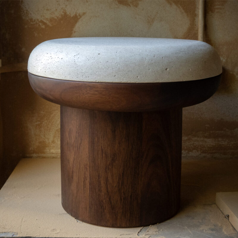 Sculptural ottoman with cylindrical natural wood base, overlapping half-circle wooden top, and polished white concrete surface